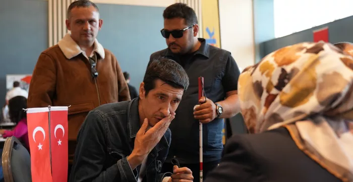 A man covering his mouth, while a blind man standing behind him, during a workshop in Turkiye